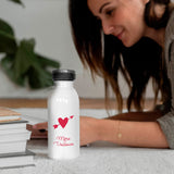 La gourde isotherme fête des mères et grands mères est présentée avec une femme à l'arrière. La gourde est personnalisée avec le message Mère Veilleuse et un cœur fléché en rouge.